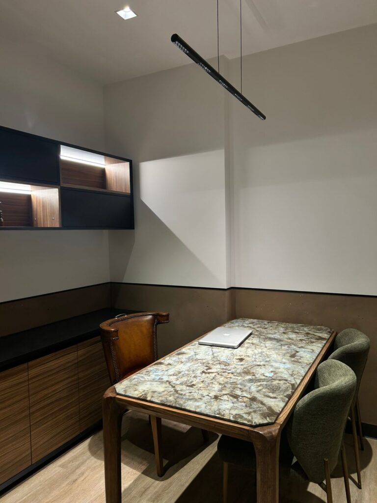 Modern office nook with a marble-topped table, brown leather chair, green upholstered chairs, and built-in wood storage cabinets.
